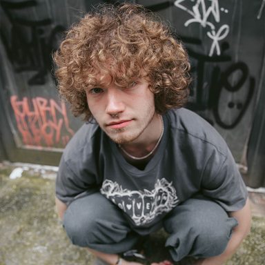 a man with curly brown hair crouches on the pavement